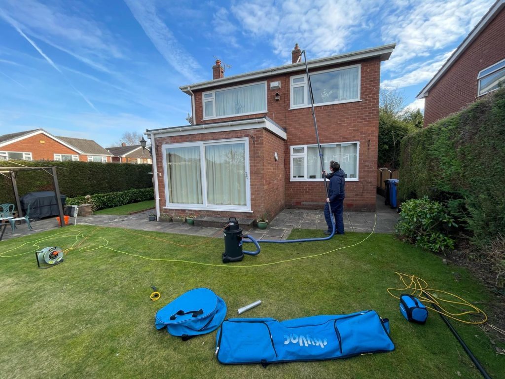 A man cleaning the gutters of a house using a gutter vac